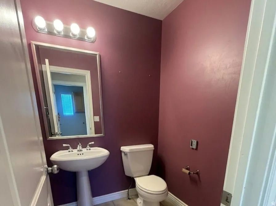 Powder room featuring a pedestal sink, white toilet, and a wall-mounted mirror with overhead lighting