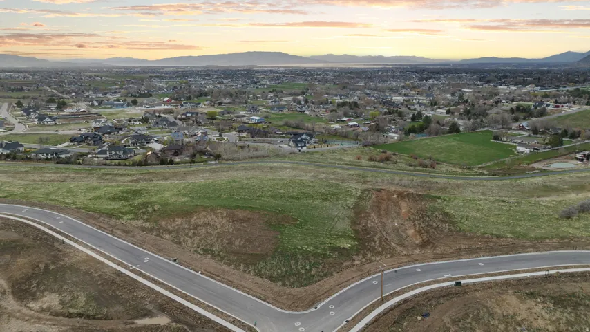 Expansive undeveloped land featuring a paved road with concrete sidewalks, established infrastructure, and distant residential areas