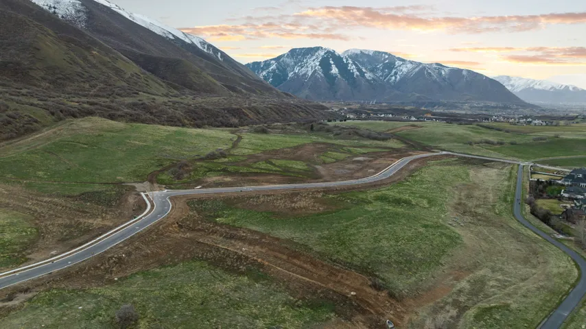 Expansive undeveloped land featuring paved roads, mountainous backdrop, and established residential areas in the distance