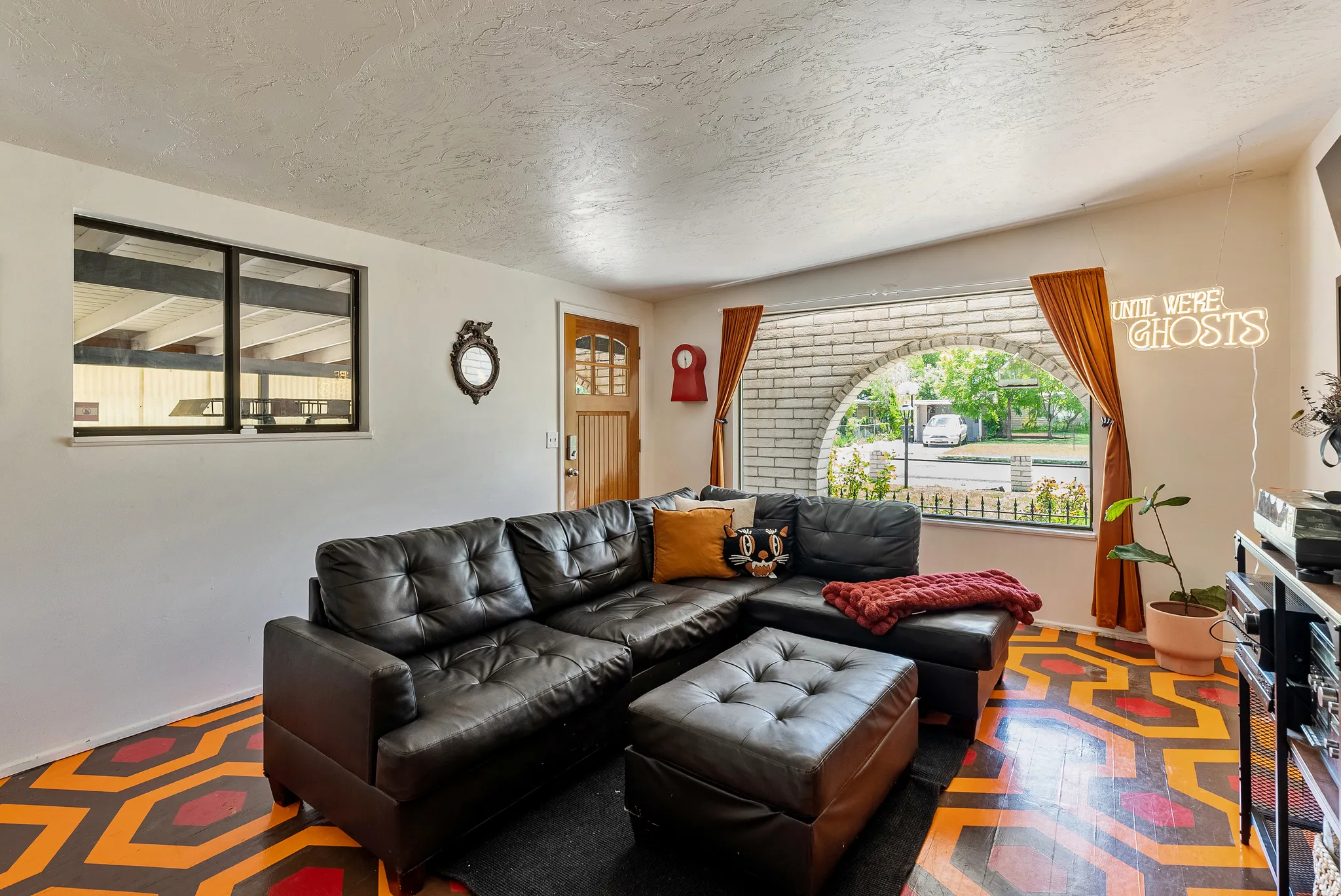 Living area featuring a distinctive geometric-patterned floor, a large arched window with brick detailing, and a multi-pane entry door