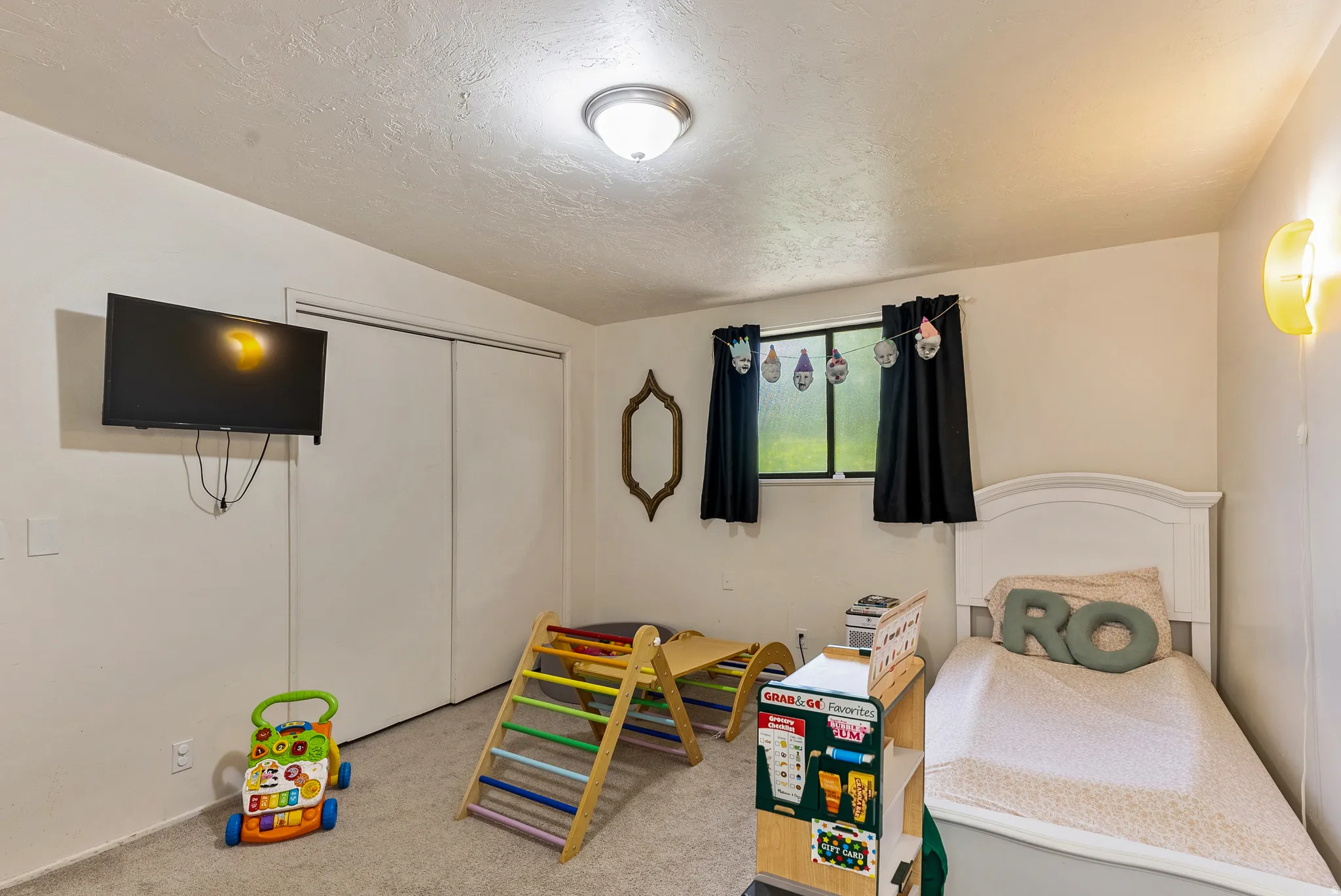 Carpeted room featuring a white paneled bed frame, a window with dark drapes, and a ceiling-mounted light fixture
