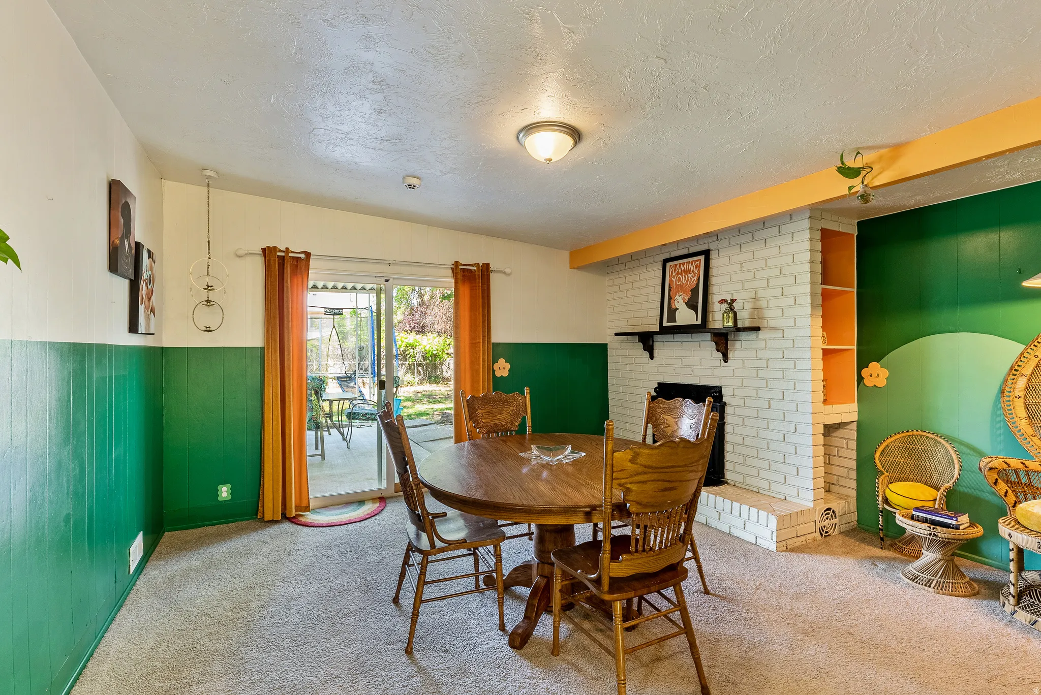Carpeted interior space featuring a white brick fireplace with a dark mantel, built-in shelving, green paneling, and sliding glass doors leading to an exterior patio