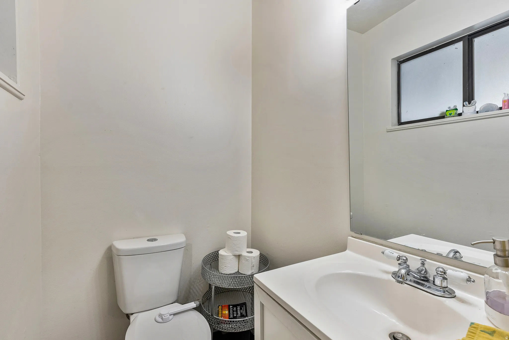 Bathroom featuring a single vanity with a white countertop and integrated sink, a chrome two-handle faucet, and a wall-mounted mirror