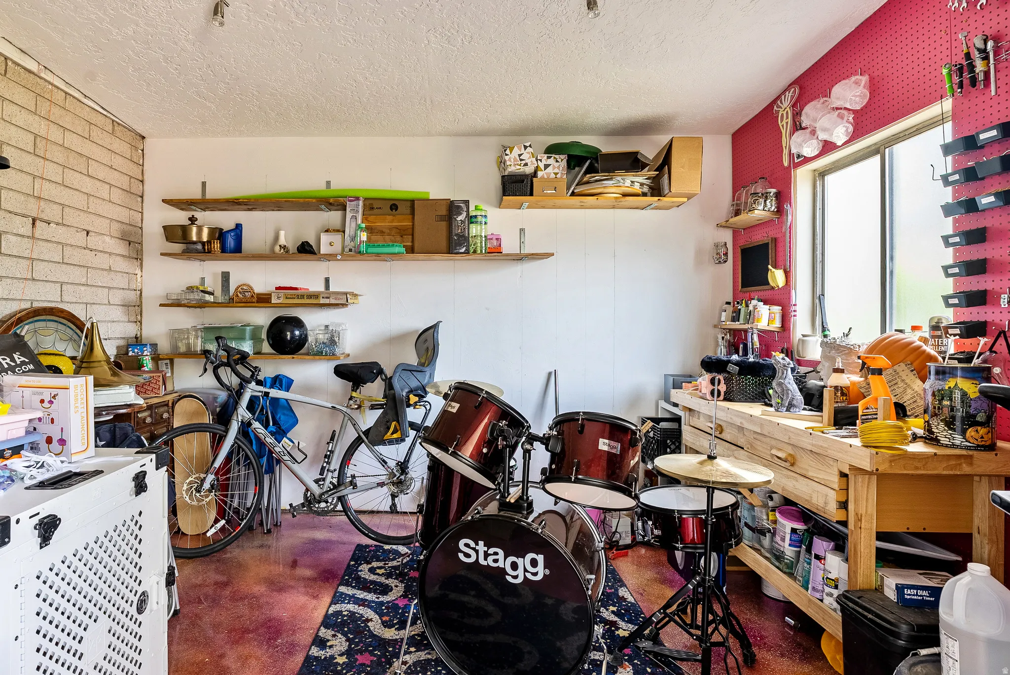 Interior room featuring exposed brick wall, multiple wood-finish shelving units, a large window, and a built-in workbench with storage