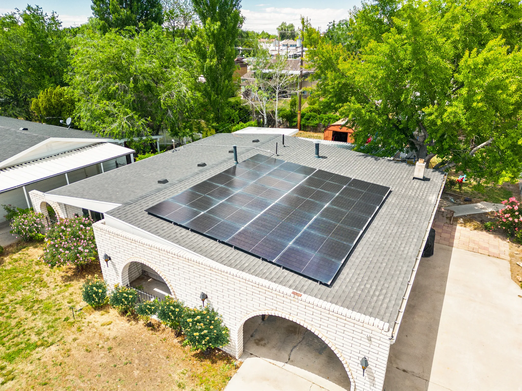 Roof-mounted solar panel array atop a light brick exterior with arched entries and a shingle roof