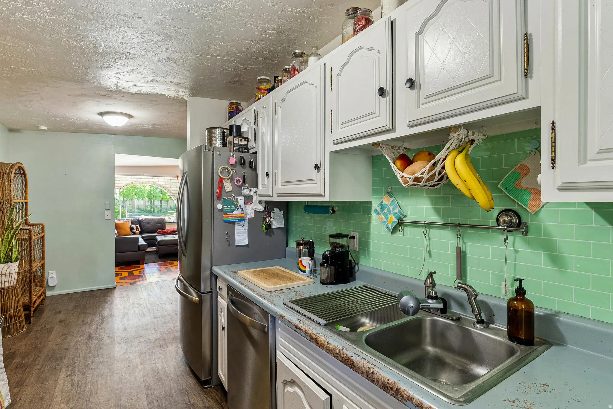 Kitchen area featuring white cabinetry, a stainless steel sink, and a mint green subway tile backsplash