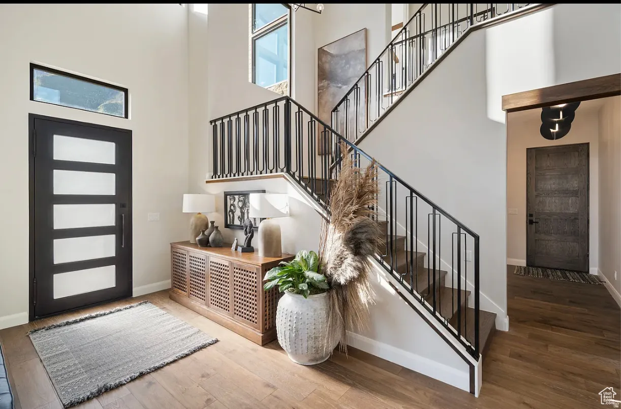 Grand entryway featuring wood-finish flooring, a contemporary staircase with black metal railings, a modern front door with frosted glass panels and an overhead transom window, and a high ceiling