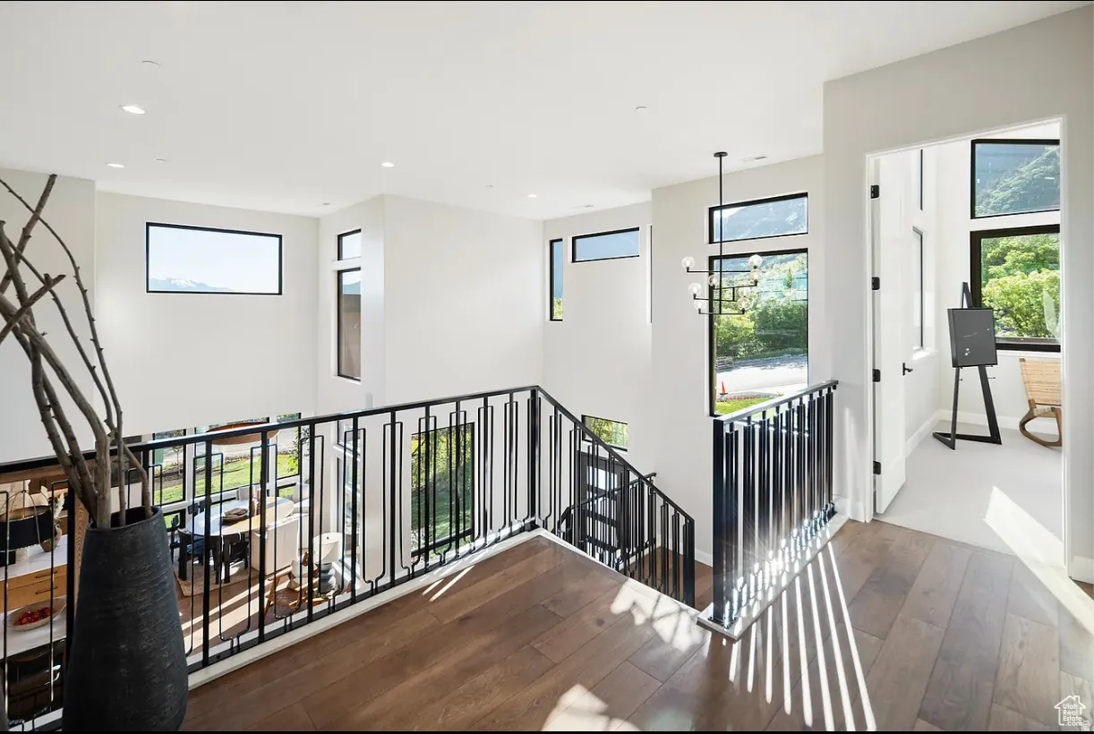 Upper-level hallway featuring wood-finish flooring and a black metal railing overlooking the lower level