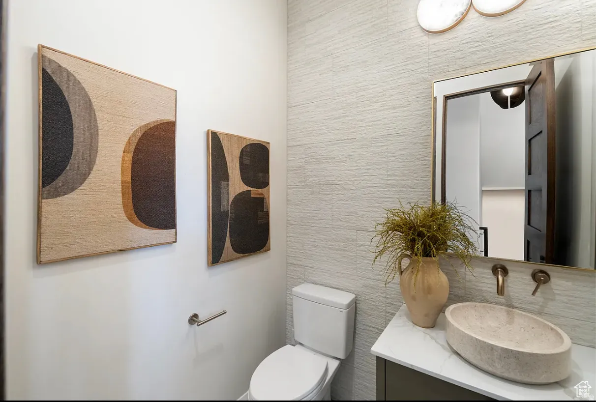 Textured accent wall, modern vanity with a stone vessel sink, and wall-mounted brass fixtures