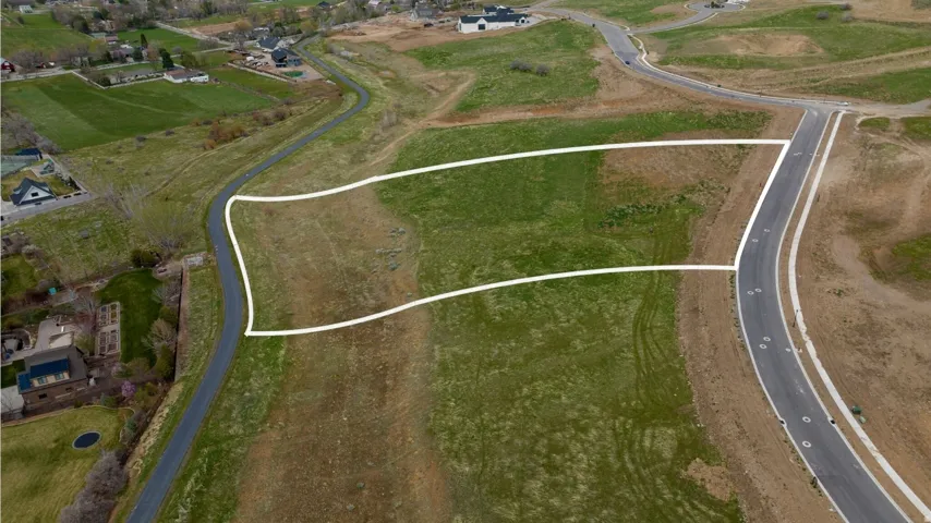 Expansive undeveloped land parcel featuring a paved road frontage, established curb cuts, and surrounding green space