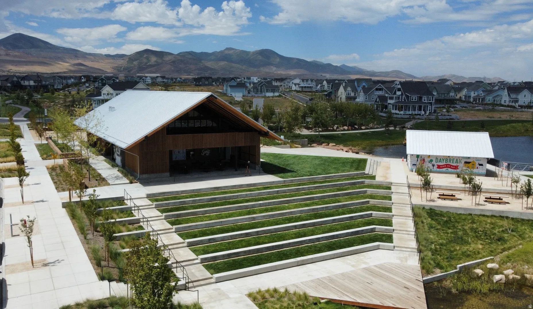 Amphitheater with terraced seating and manicured lawns, complemented by a large open-air pavilion featuring a gabled metal roof and natural wood siding