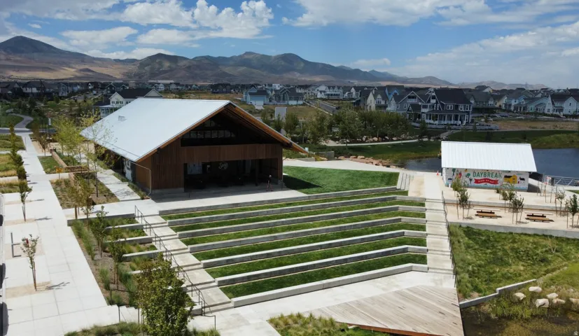 Amphitheater with terraced seating and manicured lawns, complemented by a large open-air pavilion featuring a gabled metal roof and natural wood siding
