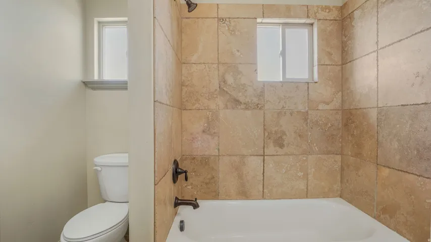 Bathtub with full-height natural stone-finish wall tiling, bronze-finish fixtures, and integrated shower head