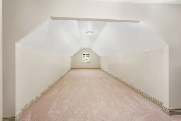Expansive carpeted room featuring sloped ceilings, a window with muntins, and recessed lighting
