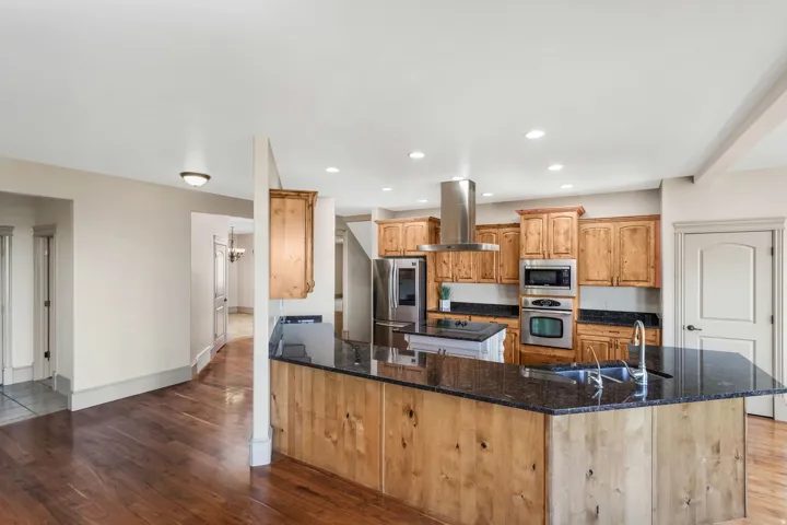 Kitchen featuring rich wood-finish flooring, light-toned cabinetry, stainless steel appliances, a range hood, and dark countertops