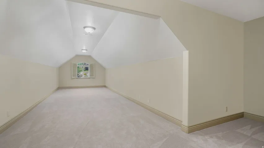 Spacious room featuring vaulted ceilings, plush carpet flooring, recessed wall niche, and natural light from a window with plantation shutters