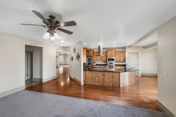 Open-concept kitchen featuring wood cabinetry, stainless steel appliances, dark countertops, and a wood-paneled island with a breakfast bar
