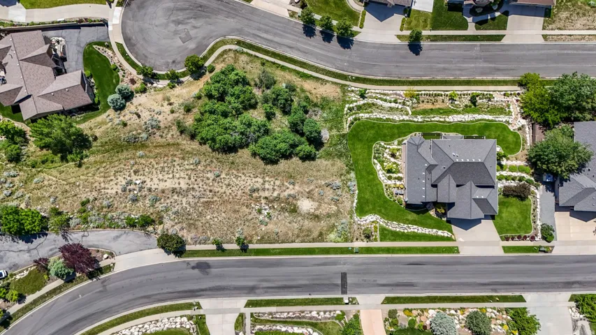 Aerial perspective showcasing a residential property with a multi-gabled dark gray roof, a concrete driveway, and surrounding green lawns