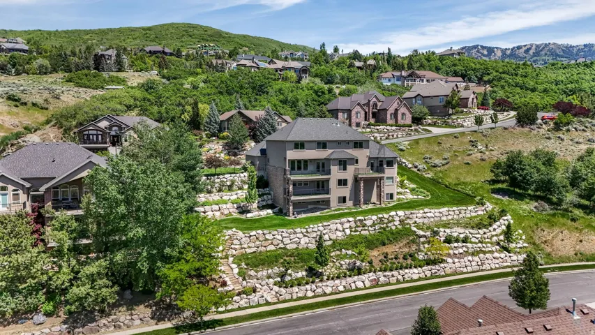 Hillside residence featuring multiple levels of stone retaining walls, terraced landscaping, a prominent balcony, and a multi-story exterior