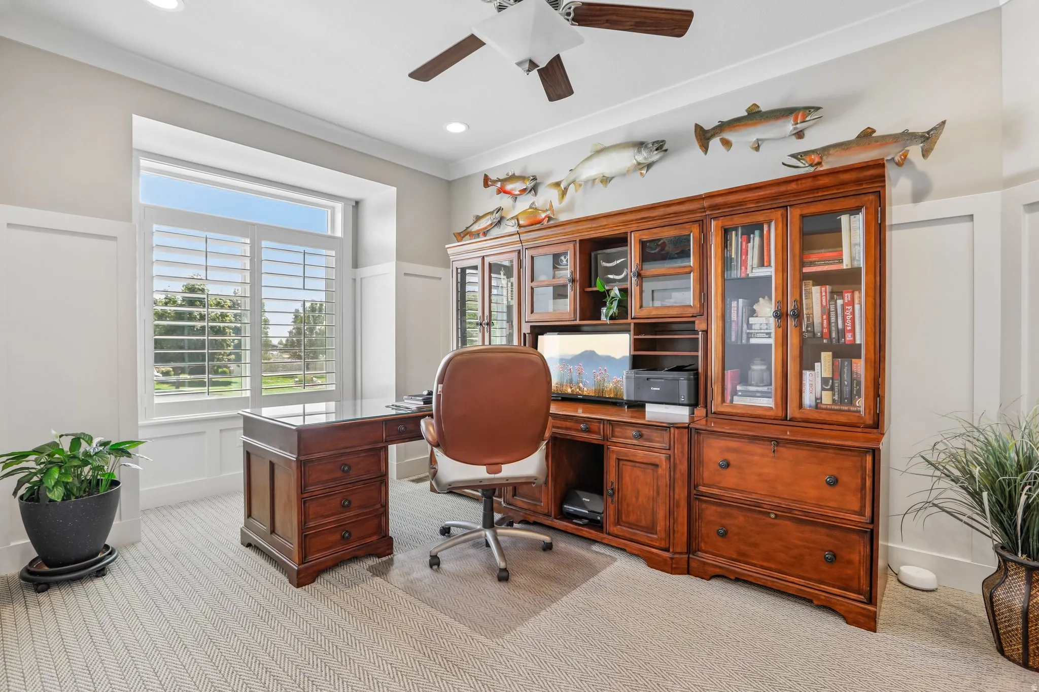 Spacious room featuring a large window with plantation shutters, custom built-in wood cabinetry, recessed lighting, a ceiling fan, and light-toned carpet flooring