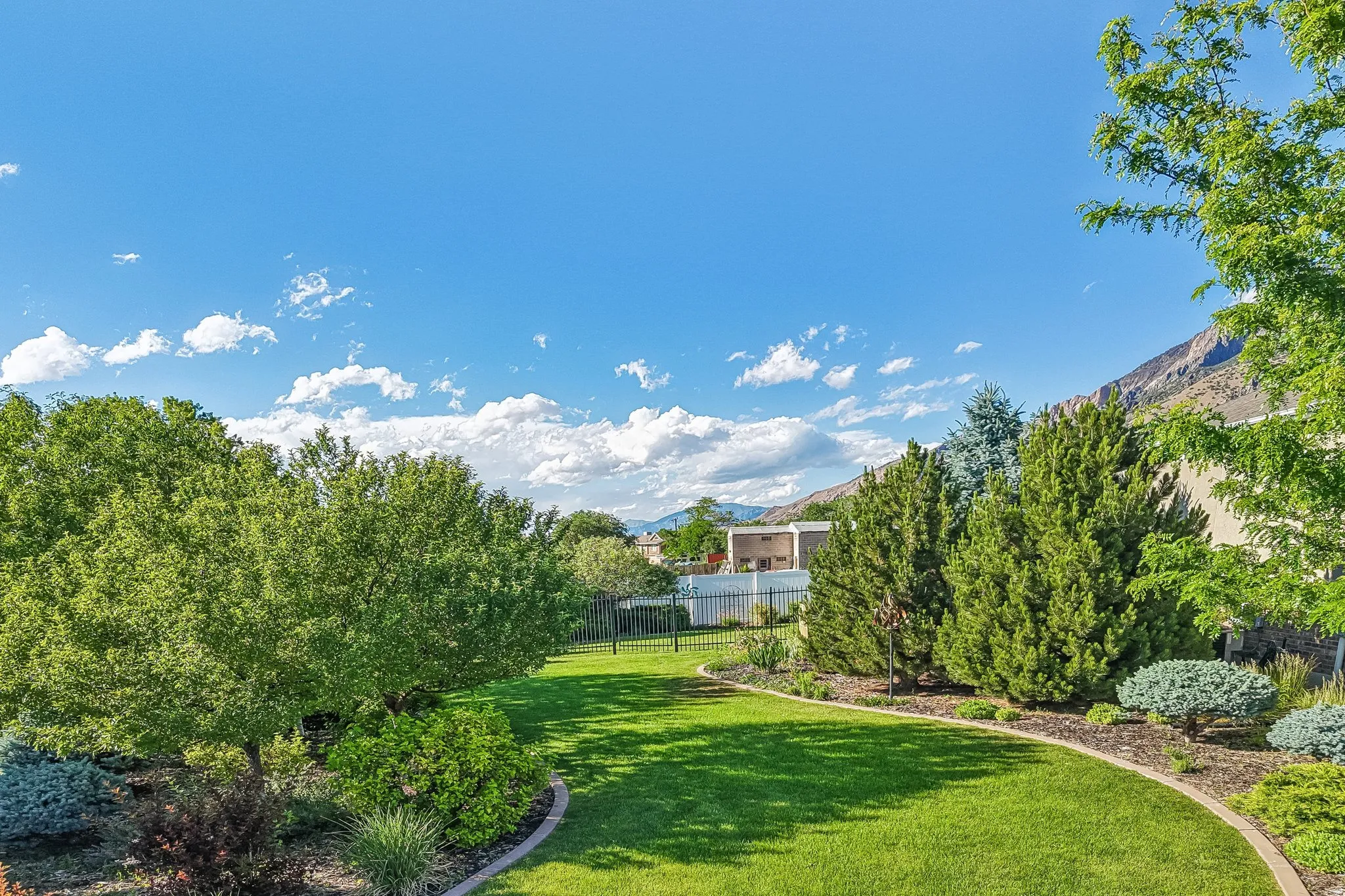Expansive backyard featuring a lush lawn, mature trees, and decorative shrubbery, fully fenced and full automatic sprinklers