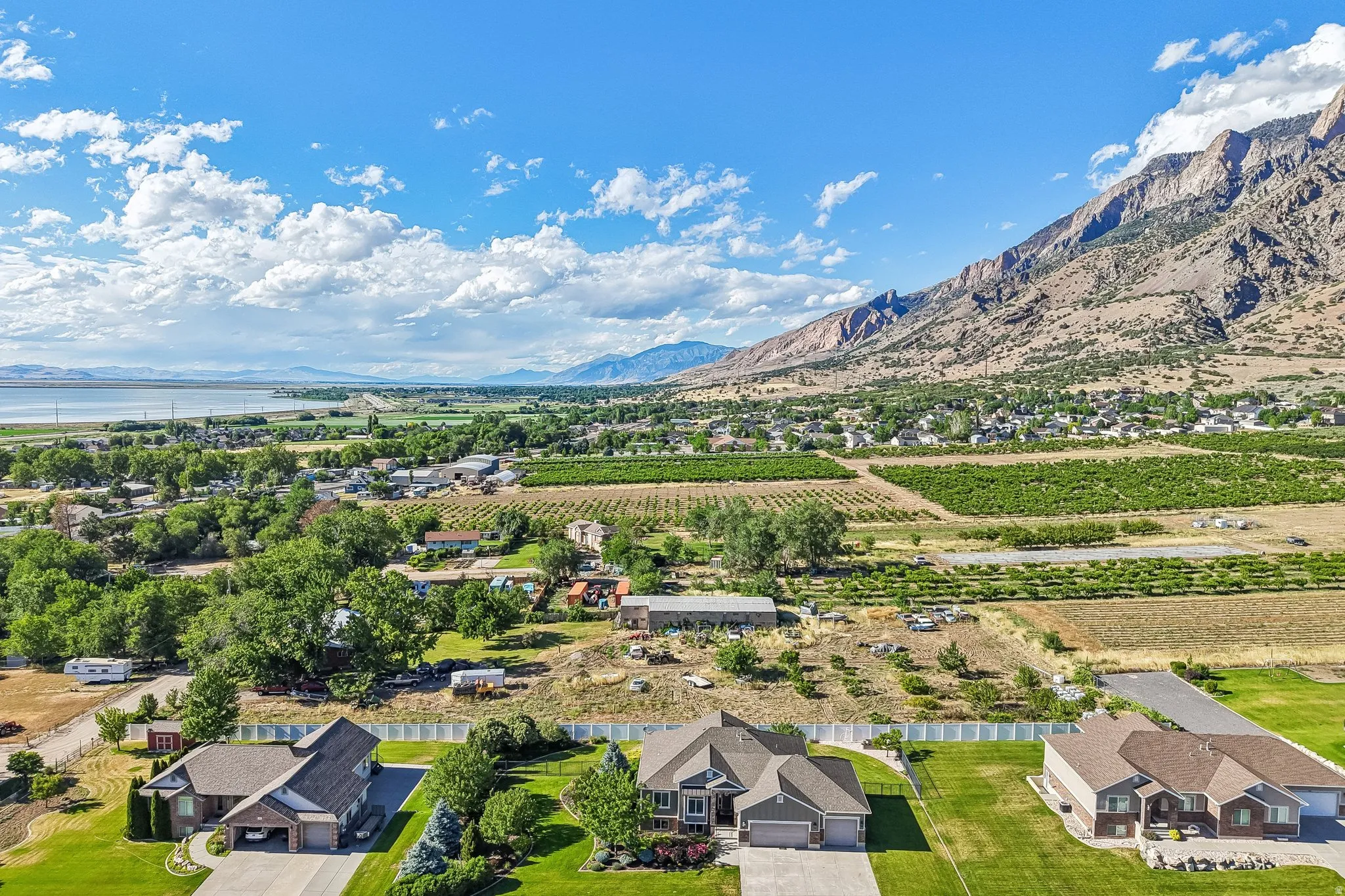 Expansive aerial perspective showcasing a residential property with a manicured lawn, a paved driveway, and an attached three-car garage, fully fenced with front custom iron fencing and back privacy fence