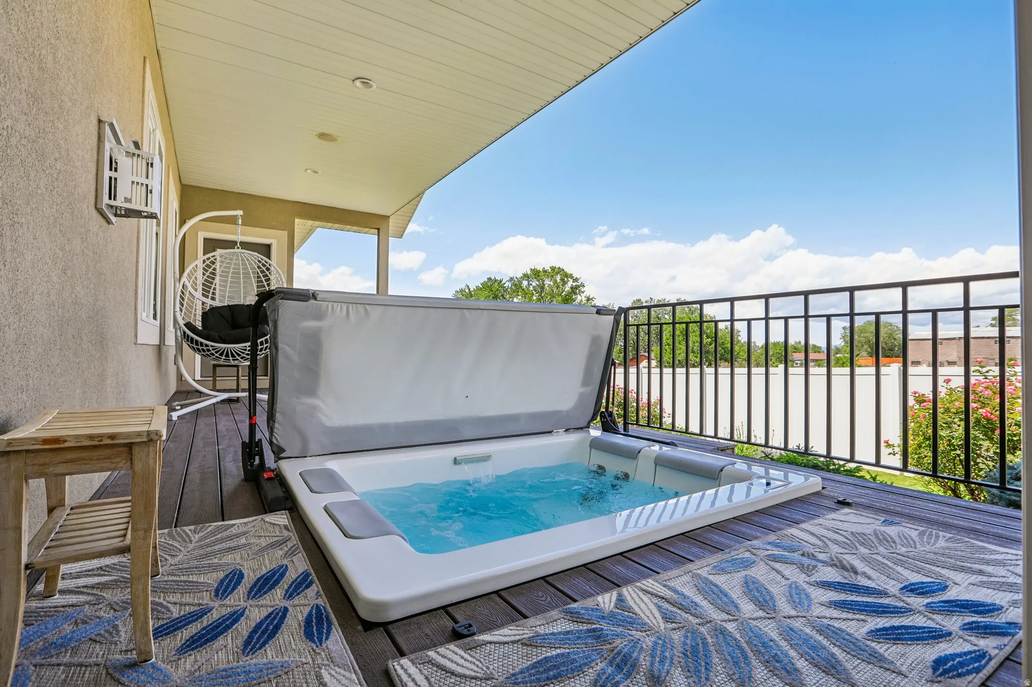 Covered outdoor deck featuring an easy to maintain Bullfrog hot-tub with secure fold down, low profile top, dark wood-finish decking, and black wrought iron railing