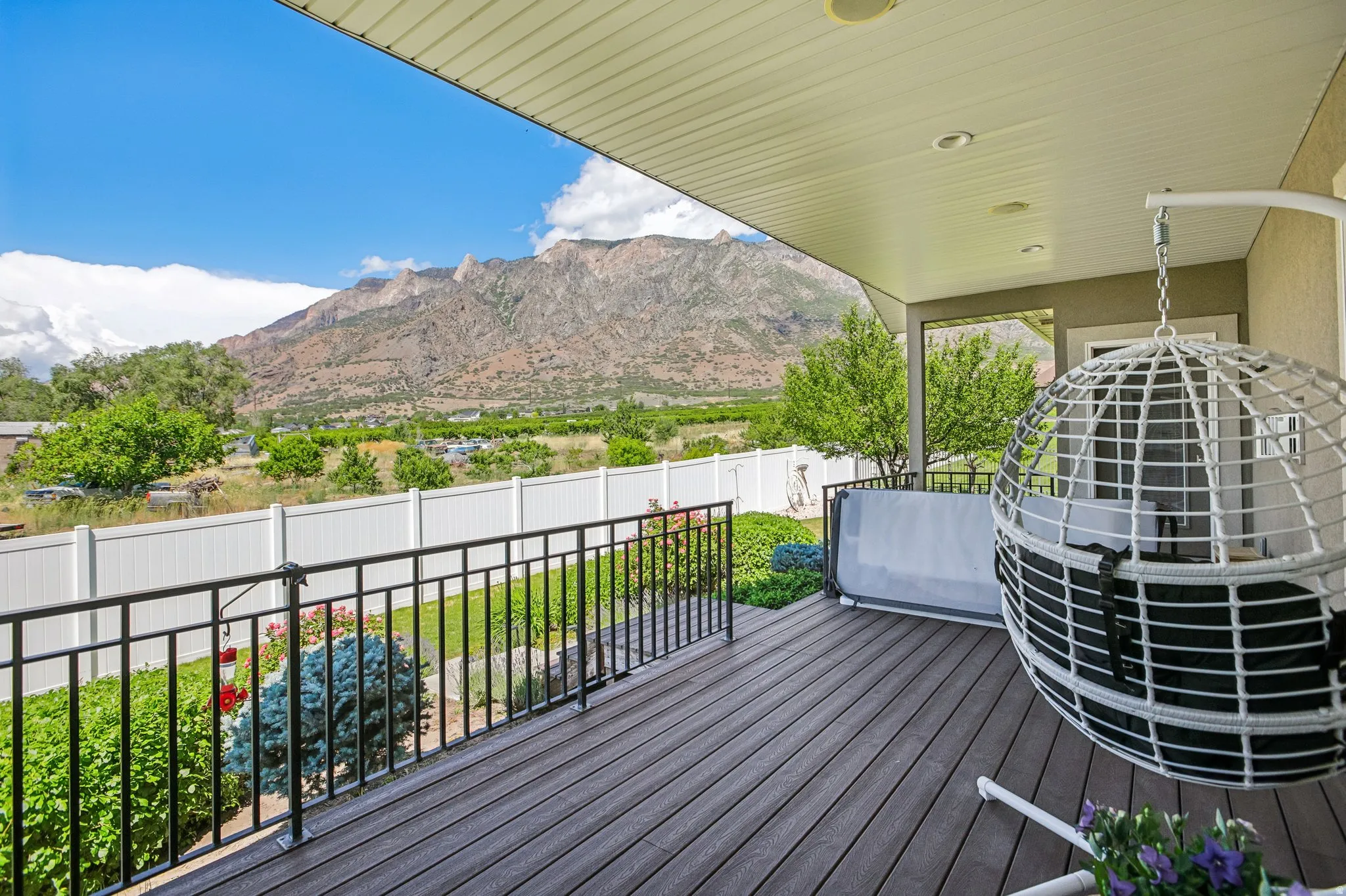 Covered outdoor deck featuring composite decking, black metal railings, recessed lighting, and a stunning prominent mountain backdrop