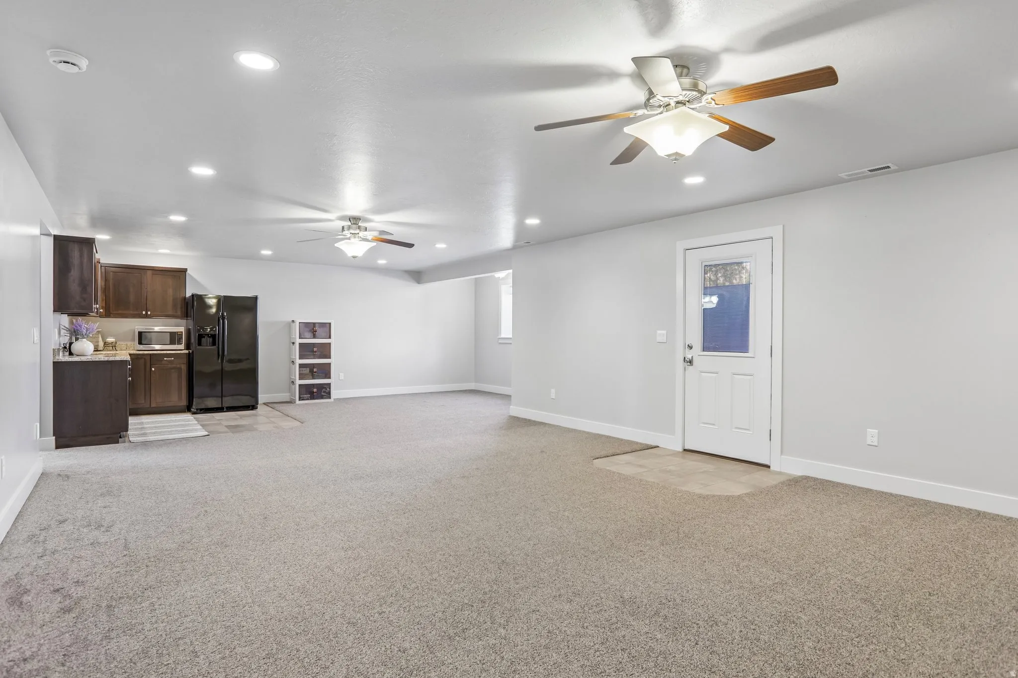 Expansive room featuring light brown carpeting, recessed lighting, and two ceiling fans and separate walk out door with atrium blind window, perfect for large entertaining or multi-generational living