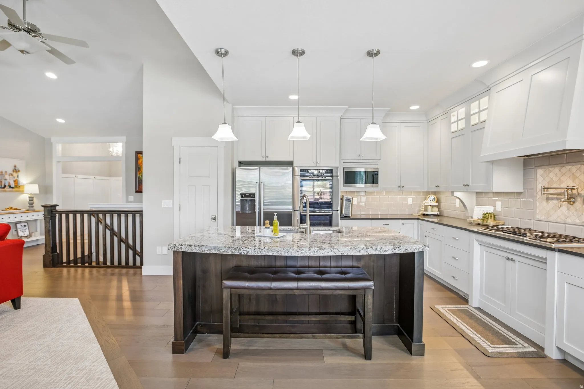 Gourmet kitchen featuring a large granite-topped island with seating, two tone cabinetry, stainless steel Bosh appliances, and wood-finish flooring
