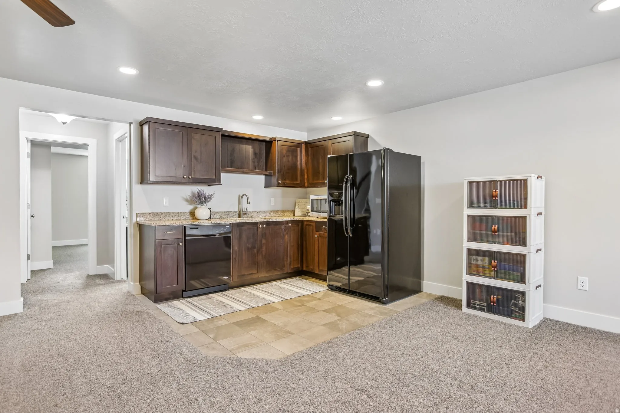 Kitchenette featuring dark wood cabinetry, a stainless steel sink with a high-arc faucet, and granite-style countertops and microwave
