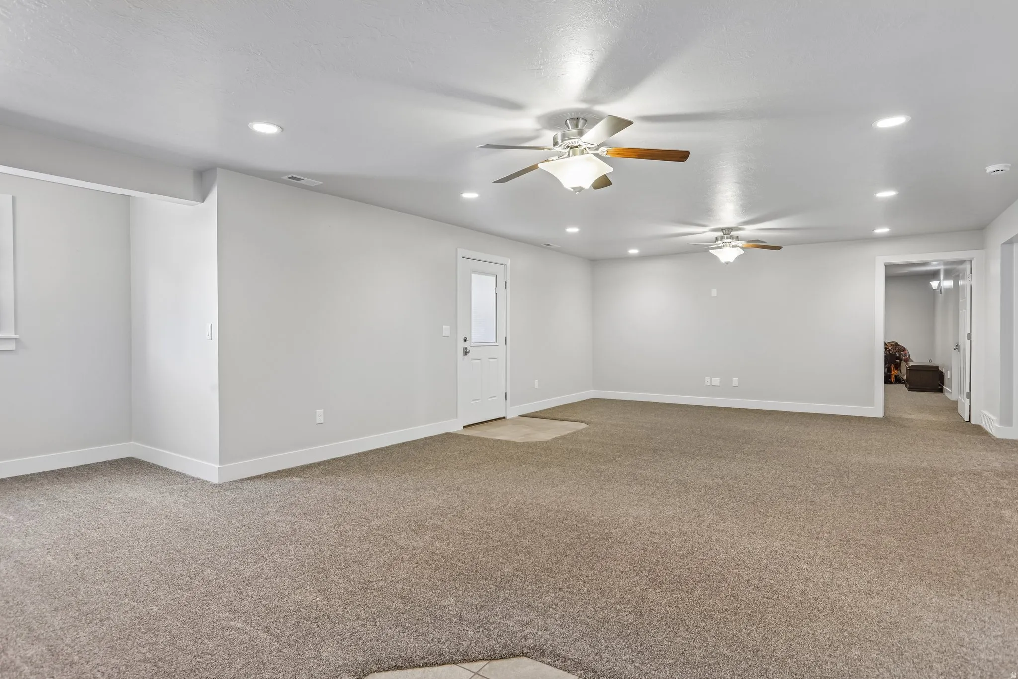 Spacious carpeted room, perfect for a pool table or ping-pong table or enough room for multi-generational living,  featuring multiple ceiling fans, recessed lighting, white baseboards, and a white door with atrium blinds and private entrance