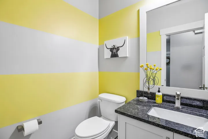 Bathroom featuring horizontal striped walls, a white vanity with a dark granite countertop, an undermount sink, and a framed wall mirror