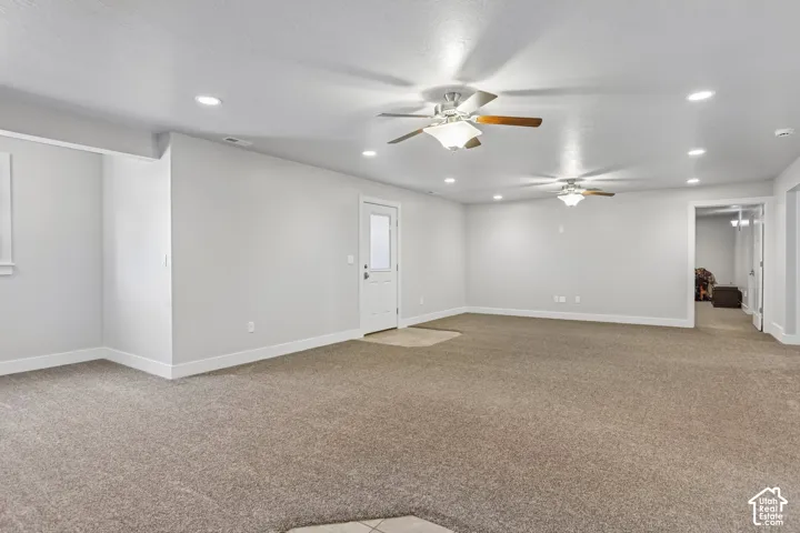 Spacious carpeted room, perfect for a pool table or ping-pong table or enough room for multi-generational living,  featuring multiple ceiling fans, recessed lighting, white baseboards, and a white door with atrium blinds and private entrance