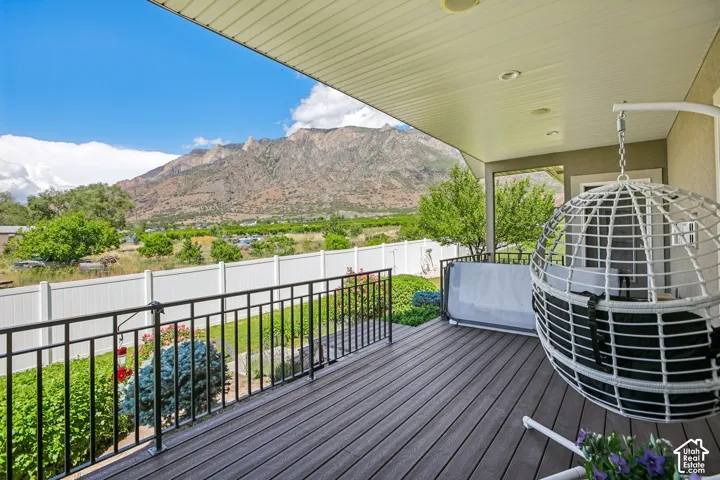 Covered outdoor deck featuring composite decking, black metal railings, recessed lighting, and a stunning prominent mountain backdrop