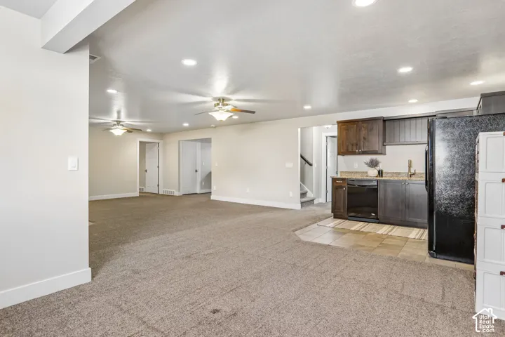 Spacious open-concept room featuring a functional kitchenette with dark wood-finish cabinetry, a black refrigerator, and a built-in black dishwasher