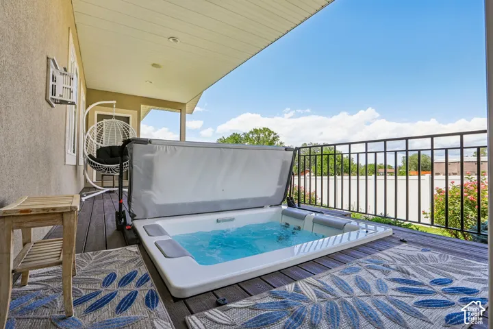 Covered outdoor deck featuring an easy to maintain Bullfrog hot-tub with secure fold down, low profile top, dark wood-finish decking, and black wrought iron railing