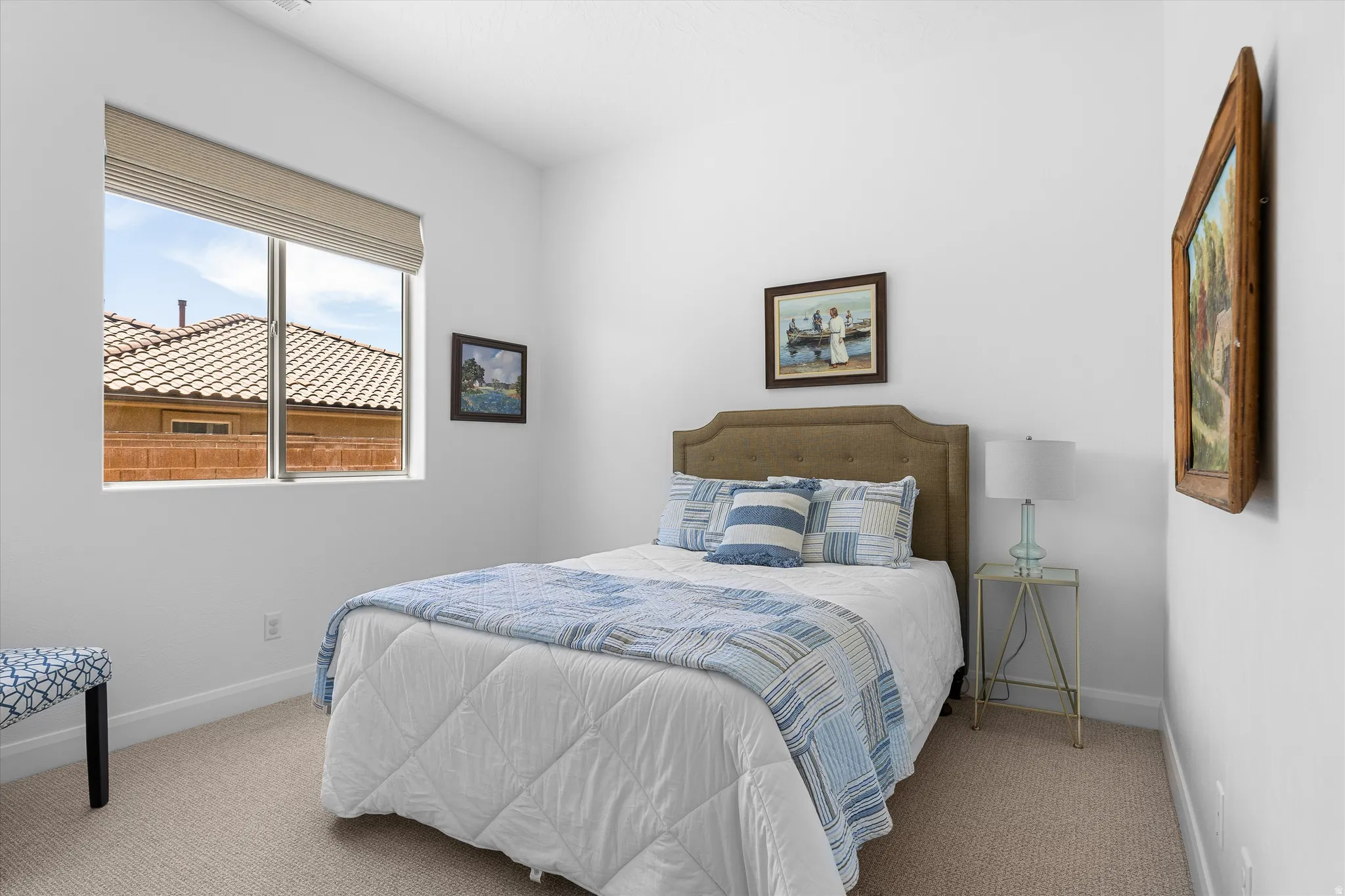 Bright room featuring a large window with a roller shade, light-colored carpeting, white baseboards, and neutral wall tones