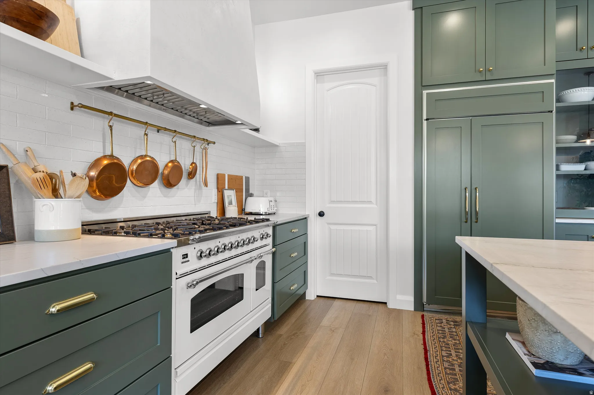 Kitchen featuring a large professional-grade range, full-height subway tile backsplash, custom green cabinetry with brass hardware, a built-in paneled refrigerator, and wood-finish flooring