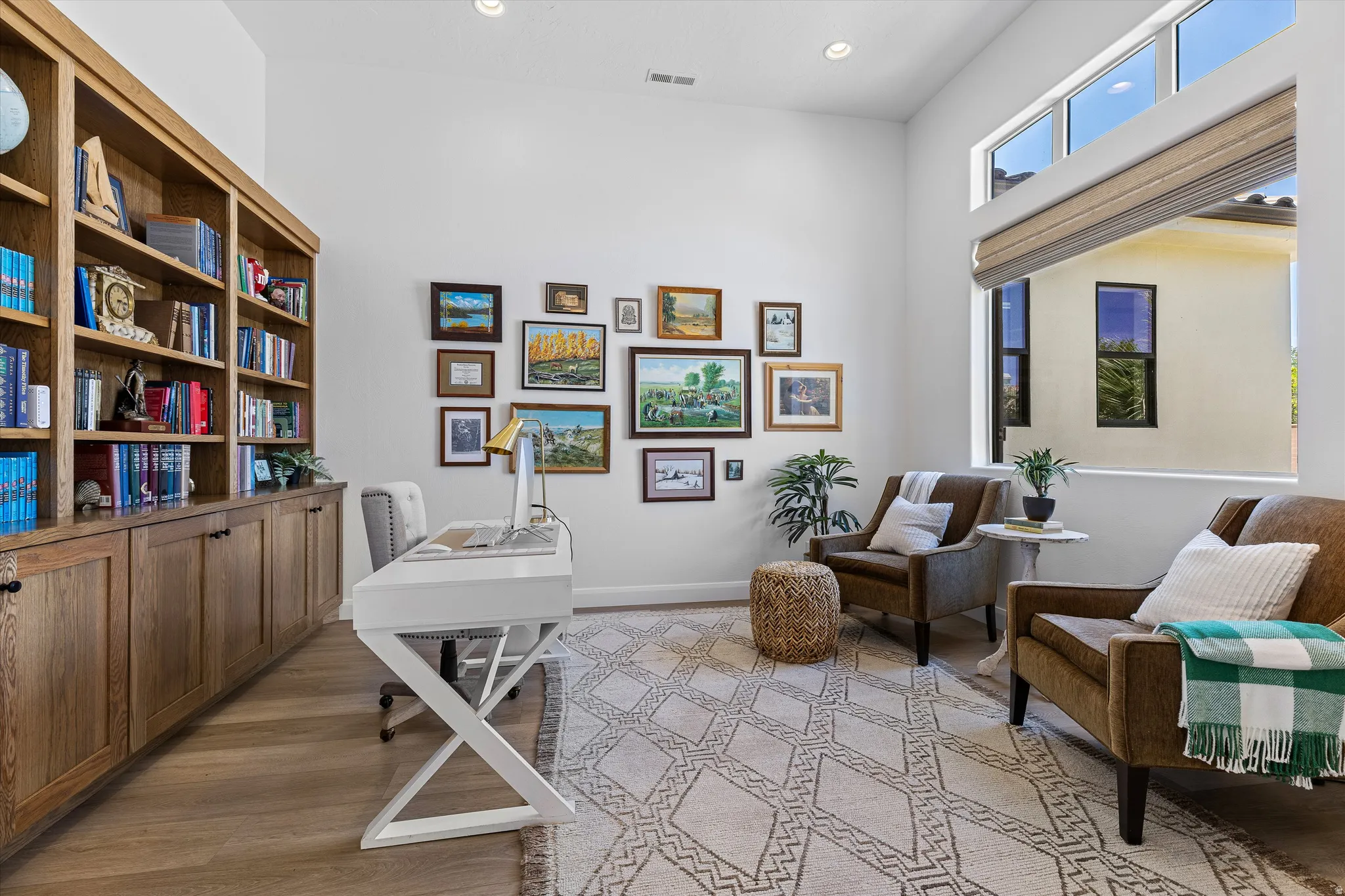 Dedicated office space featuring built-in wood cabinetry with integrated shelving, wood-finish flooring, and high ceilings