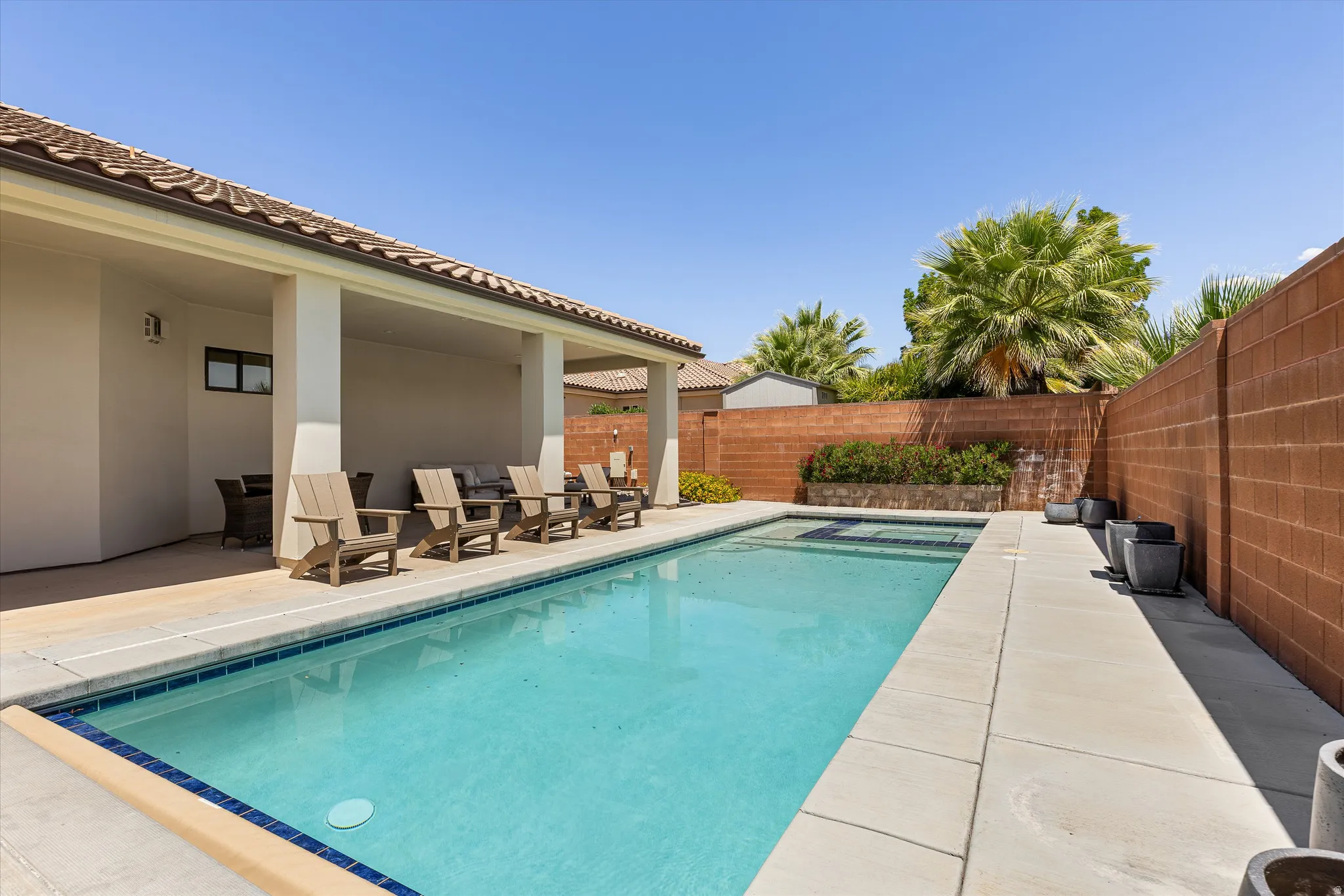 Private backyard featuring a rectangular swimming pool with integrated spa, concrete decking, and a covered patio area