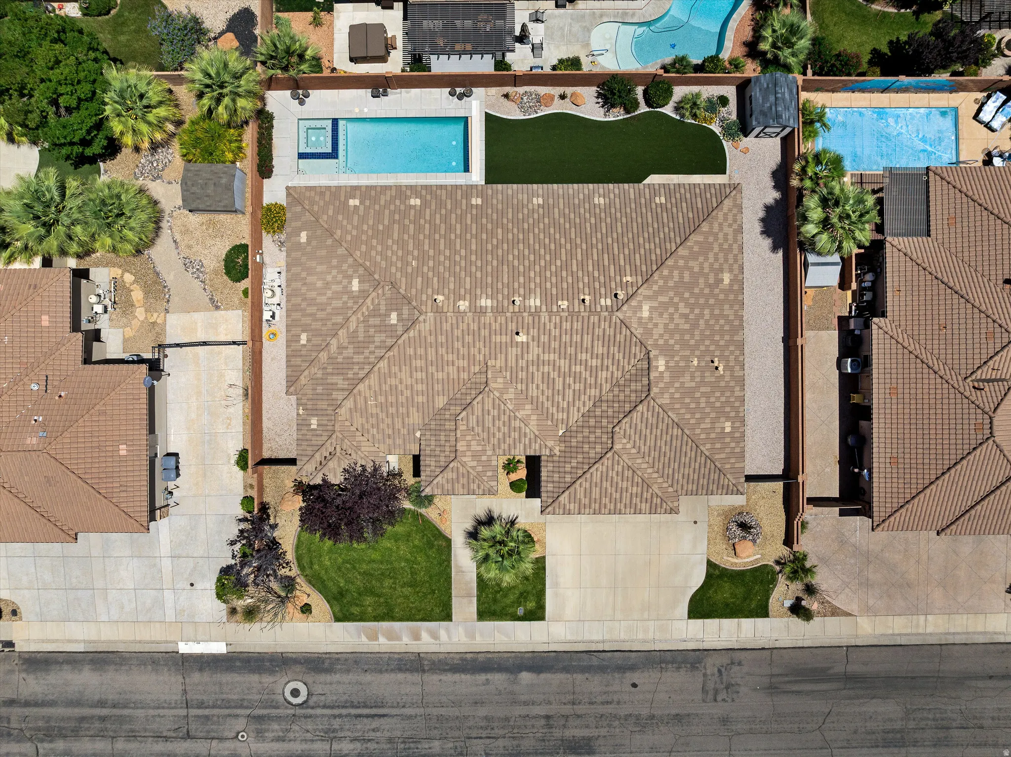 Aerial property overview showcasing a residential roofline, a private swimming pool with integrated spa, a paved patio, and a section of artificial turf