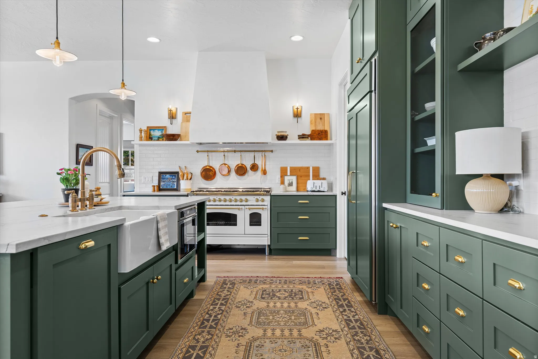 Kitchen featuring dark green cabinetry, a white farmhouse sink, a large central island with seating, brass hardware, and a white range with a matching hood