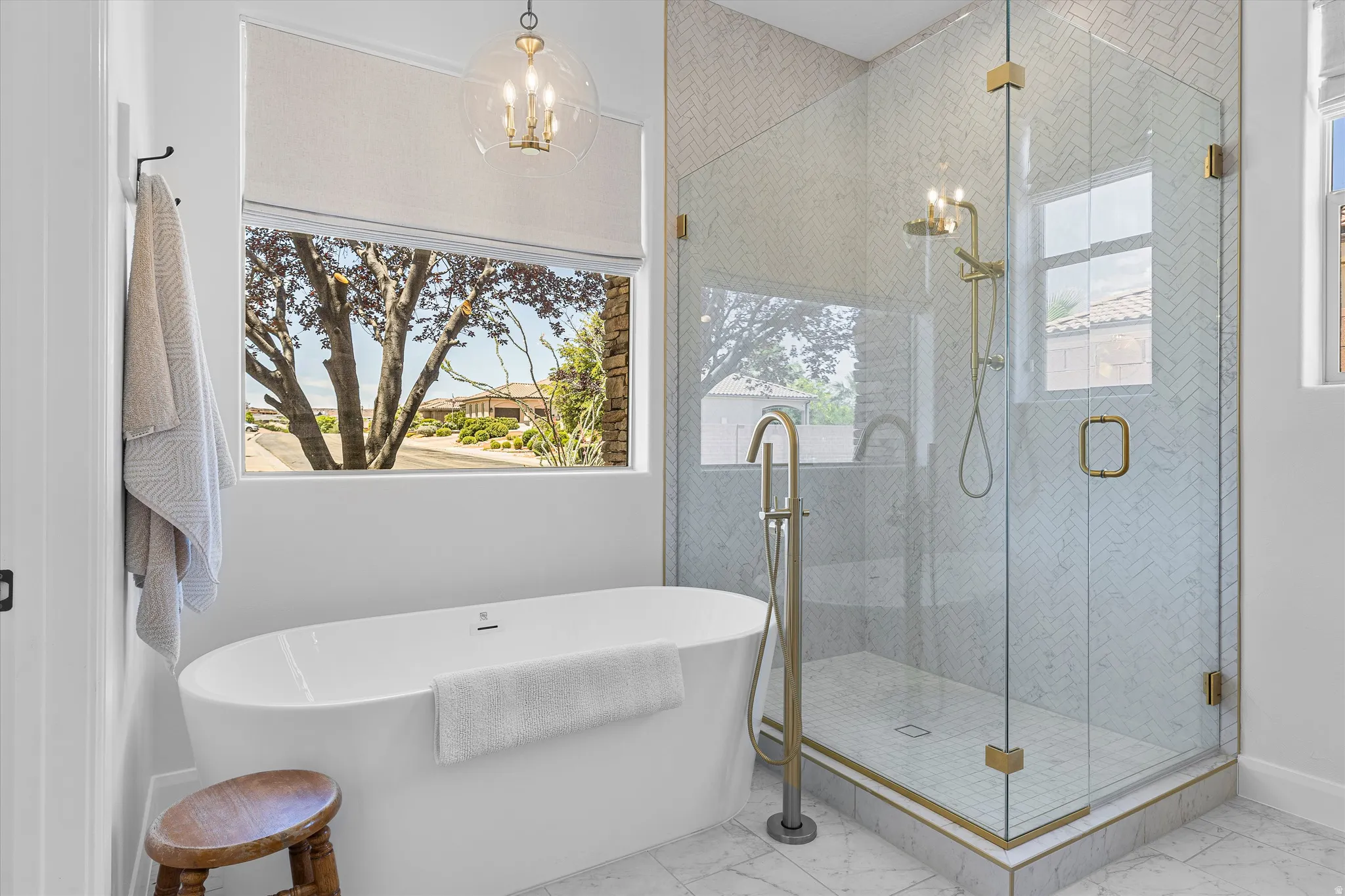 Freestanding soaking tub with a floor-mounted brass faucet, alongside a glass-enclosed shower featuring herringbone tile and brass fixtures
