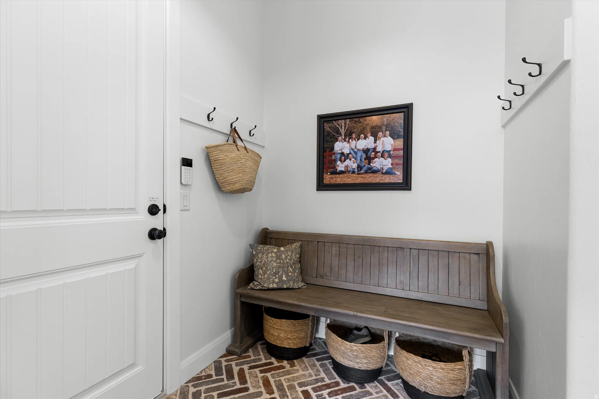 Entry area featuring herringbone brick-pattern flooring, a white paneled door with black hardware, and a built-in coat rack with black hooks