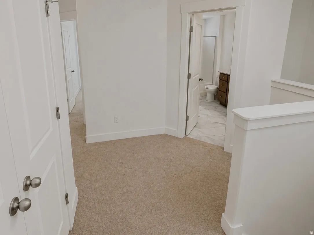 Carpeted landing area featuring a doorway to a bathroom with tile flooring, a dark wood-finish vanity, and a toilet