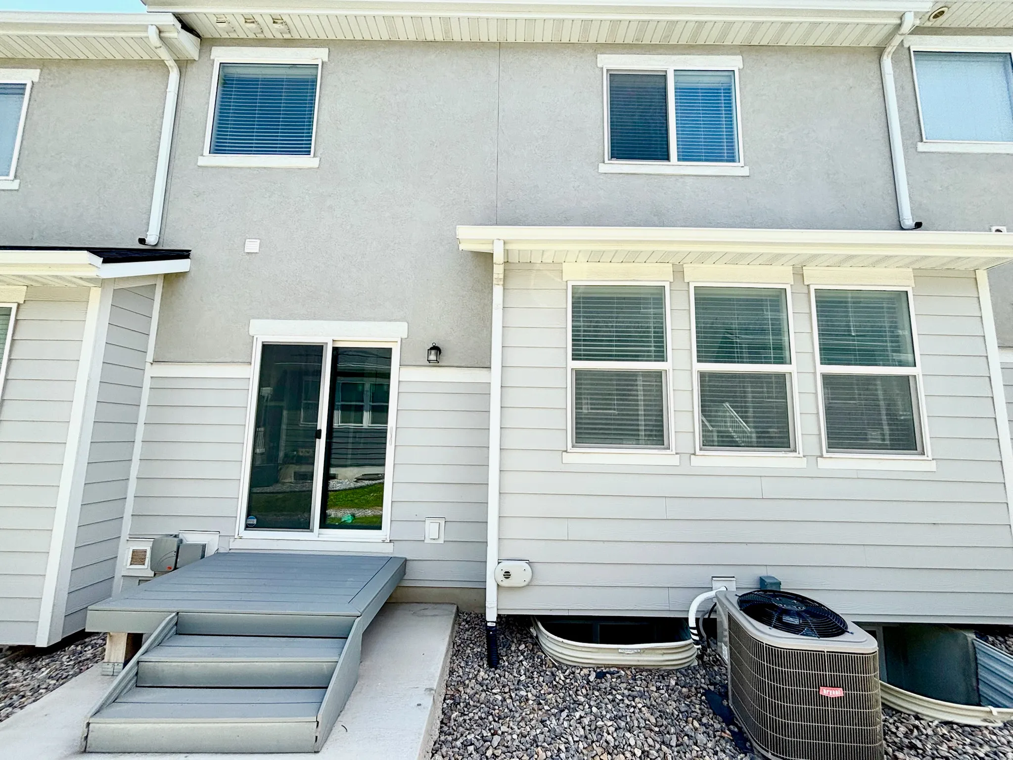 Rear exterior featuring a composite deck with stairs, sliding glass door, and a stucco and siding facade