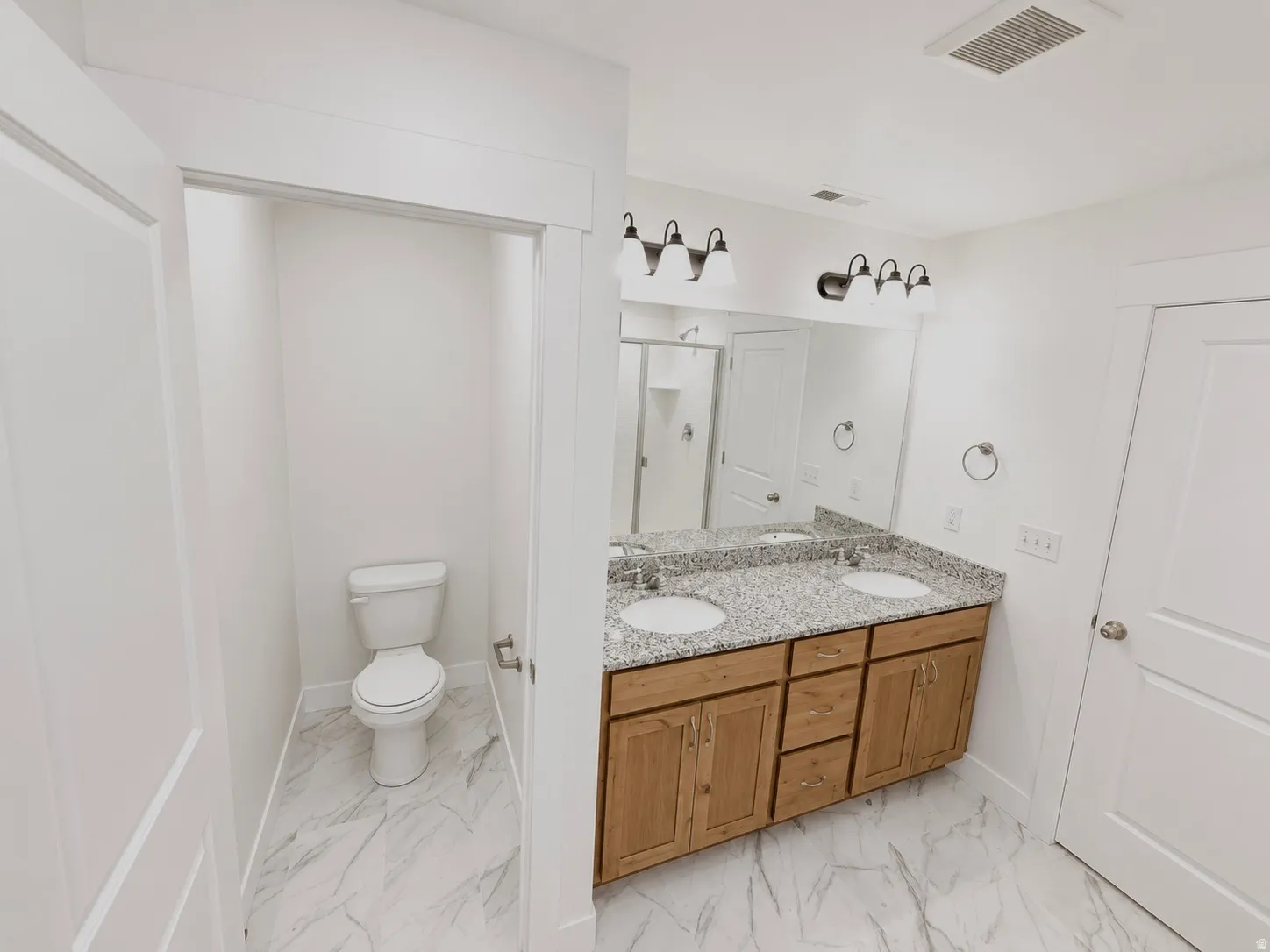 Bathroom featuring a dual vanity with granite countertop, wood-finish cabinetry, and undermount sinks