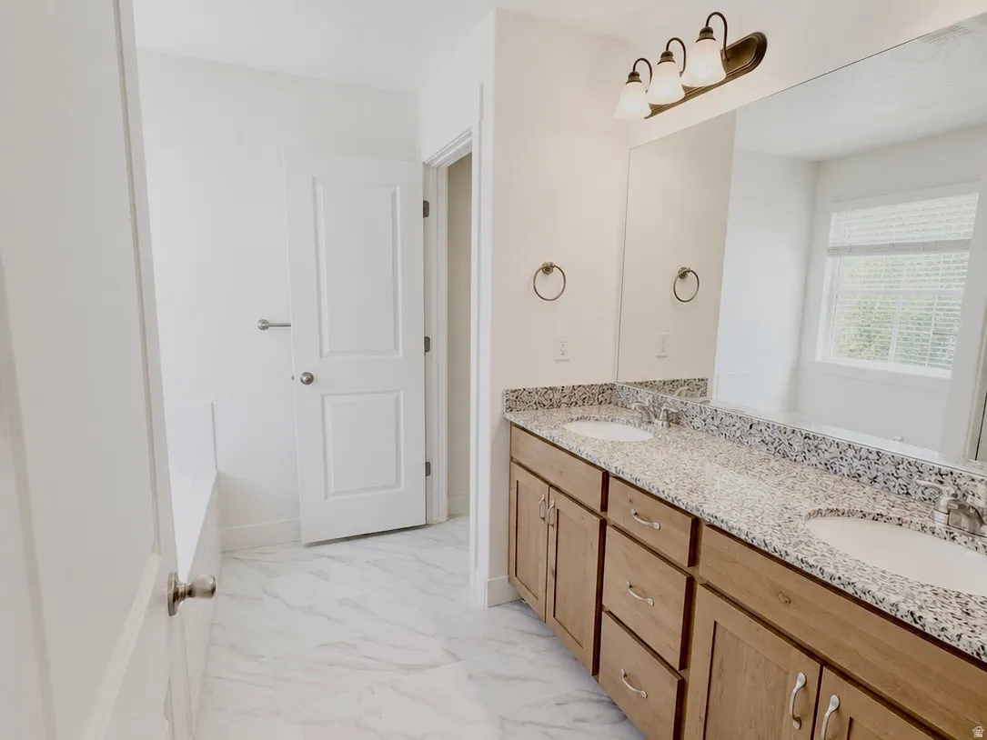 Bathroom featuring a double vanity with stone-finish countertop, wood-finish cabinetry, and undermount sinks