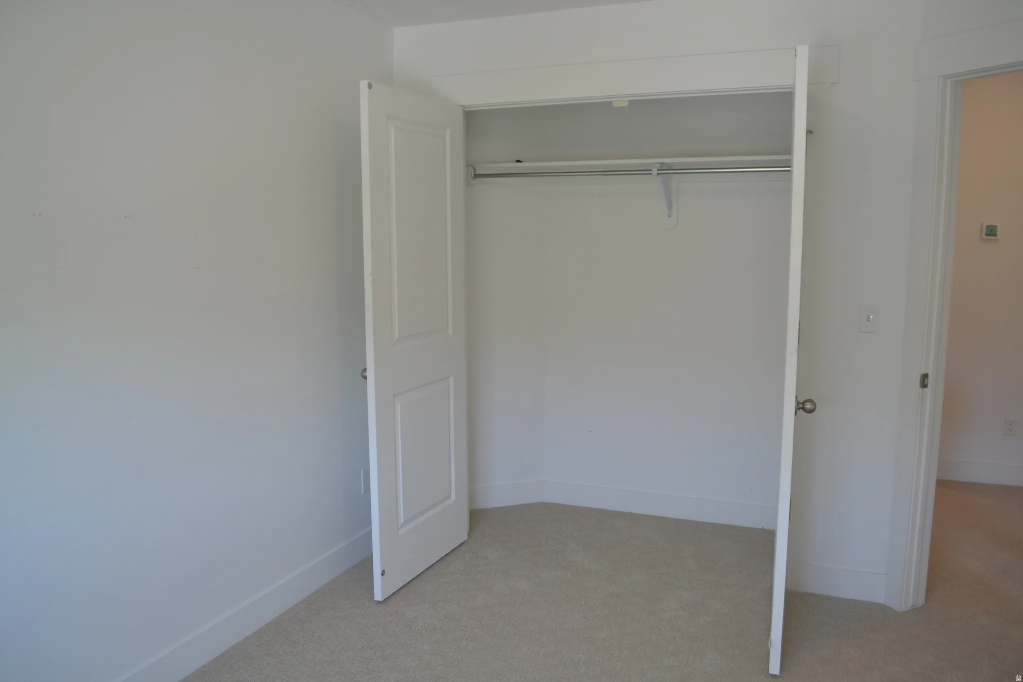 Built-in closet with double white panel doors, chrome hanging rod, and light beige carpet flooring